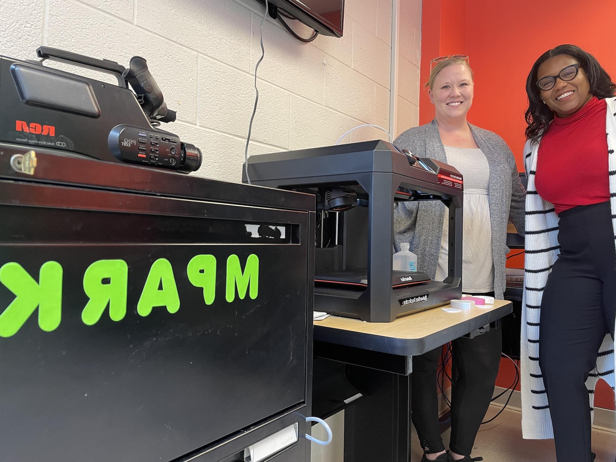 研究生 teaching assistants Lamaya Williams 和 Emily Ivey st和 next to mpark’s 3D printer.